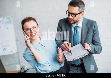 Geschäftsmann bitten, seine Kollegin Dokument zu unterzeichnen, während Sie am Telefon sprechen und ihm lästige Stockfoto