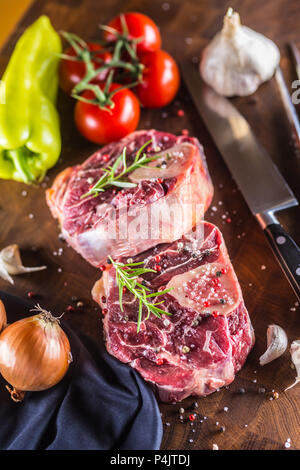 Zwei Stücke rohes Rindfleisch Schaft und Grundstoffe auf gulasch - Zwiebel Pfeffer Tomaten Knoblauch Salz Gewürze und Rosmarin. Stockfoto