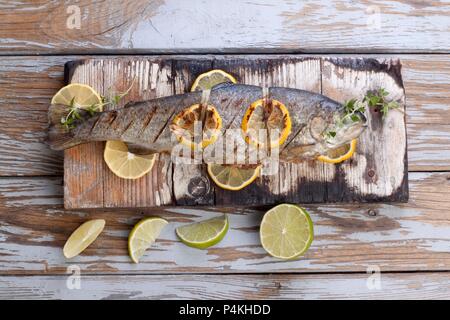 Gegrillte Forelle mit Zitronen und Limetten auf einem Holzbrett Stockfoto