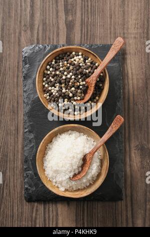 Schwarzer und weißer Pfeffer und grobem Meersalz mit Löffeln in kleinen Schüsseln Stockfoto