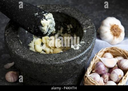 Gestampften Knoblauch in grauem Granit Mörser mit Pistill, stehend auf dunklen Blech Stockfoto