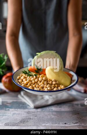 Eine Frau mit einer Schüssel mit Kichererbsen, Kartoffeln, Karotten und Kohl (Zutaten für Cocido madrileno - ein spanischer Eintopf) Stockfoto