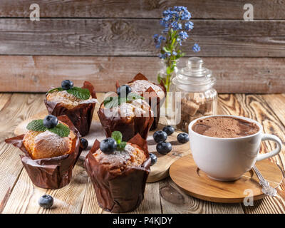 Muffins mit Heidelbeeren und eine Tasse heiße Schokolade auf einem hölzernen Hintergrund. hausgemachte Backen Stockfoto
