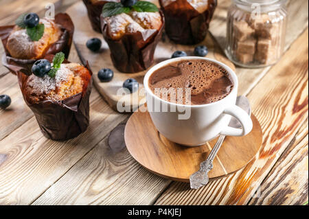 Muffins mit Heidelbeeren und eine Tasse heiße Schokolade auf einem hölzernen Hintergrund. hausgemachte Backen Stockfoto