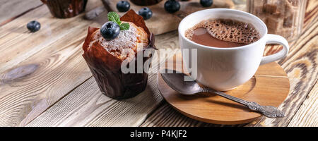 Muffins mit Heidelbeeren und eine Tasse heiße Schokolade auf einem hölzernen Hintergrund. Hausgemachte backen. Banner Stockfoto