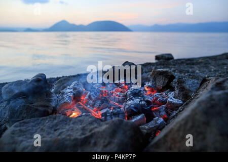 Glühende Asche Schwelbrand in einem Stein Feuer Ring am Ufer des Sees Koya in Hokkaido, Japan Stockfoto