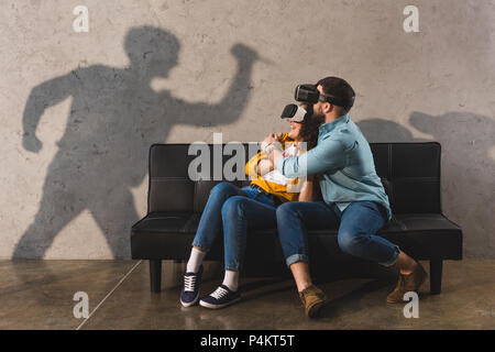 Schatten der Mann mit Messer und erschrocken Paar in virtual reality Headset auf der Couch Stockfoto
