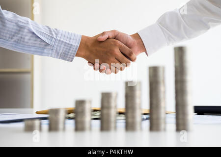 Zwei Menschen schütteln Hand mit gestapelten der Münze auf Holz Tisch Konzept wie Kooperation und Teamwork zum Erfolg im Geschäft und finanziellen Stockfoto