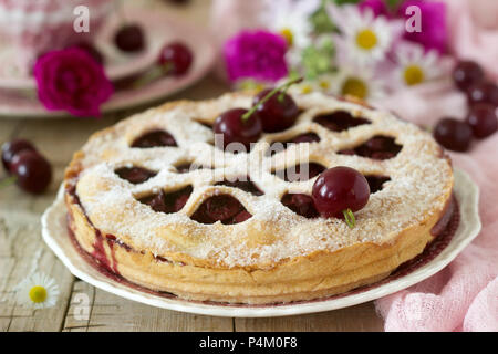 Eine Cherry Pie mit Herzen verziert-förmige Verzierungen mit einer Tasse Tee, einem Blumenstrauß und reife Kirsche Beeren. Vintage Style, selektiver Fokus Stockfoto