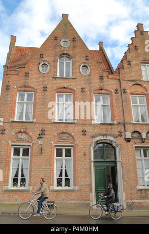 Brügge, Belgien - 18 April 2014: Radfahrer reiten entlang der traditionellen Fassaden Stockfoto