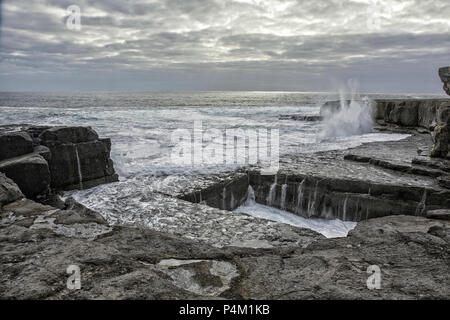 Klippen Loch im Felsen benannt das Wurmloch auf Aran Islands, Irland mit Spritzwasser im Hintergrund und dramatische Lichteffekte Stockfoto