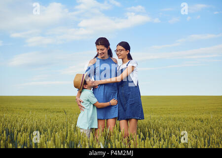 Eine Mutter umarmt mit Kindern in einem Feld von Weizen in der Natur. Stockfoto