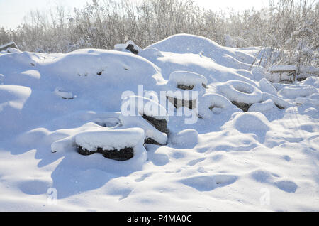 Benutzt und weggeworfen Autoreifen liegen auf der Seite der Straße, mit einer dicken Schicht Schnee bedeckt. Stockfoto
