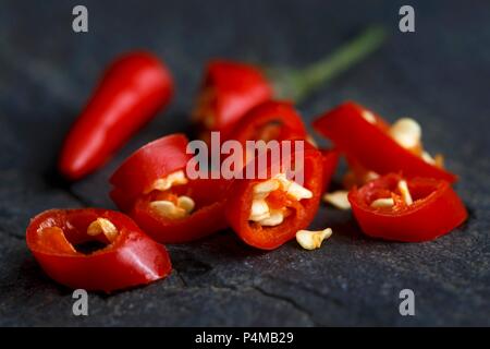 Schneiden Sie frisches Birds Eye Chili mit Samen auf dunklem Schiefer Hintergrund. Stockfoto