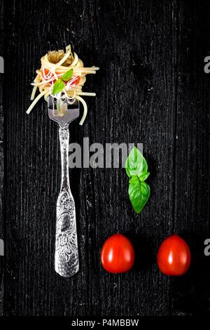 Italienische Pasta mit Tomaten und Basilikum auf Gabel auf Holzbrett Stockfoto