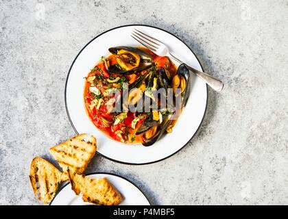 Gedünsteter Neu-england Miesmuscheln in Tomaten geschmort mit einer Seite der gegrillten Sauerteig Brot serviert. Stockfoto