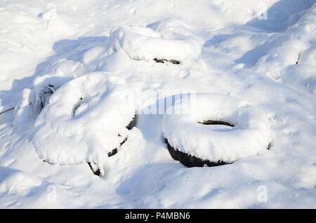 Benutzt und weggeworfen Autoreifen liegen auf der Seite der Straße, mit einer dicken Schicht Schnee bedeckt. Stockfoto