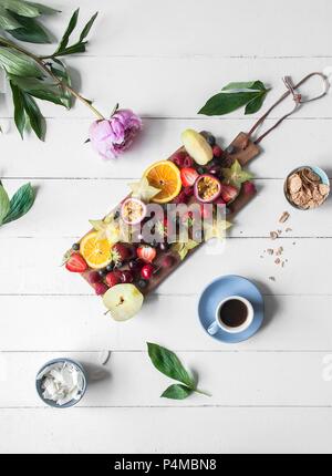 Verschiedene frische Früchte serviert auf einem Holzbrett und einer Tasse Kaffee Stockfoto