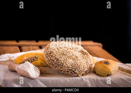 Verschiedene frische Brotsorten auf einem alten Holztisch mit Mehl und eine Serviette Stockfoto