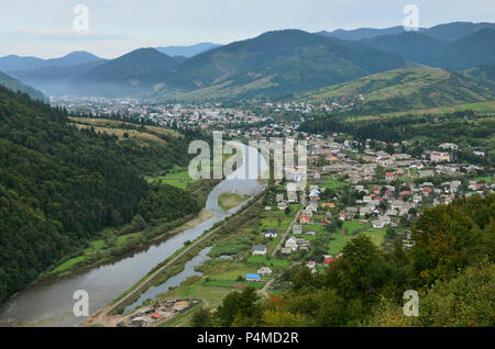 Eine wunderschöne Aussicht auf das Dorf Mezhgorye, Karpaten Region. Eine Menge von Wohngebäuden durch hohe Wald Berge und lange Fluss umgeben Stockfoto