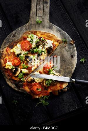 Eine geschnittene vegetarische Pizza auf einer hölzernen pizza Paddel Stockfoto