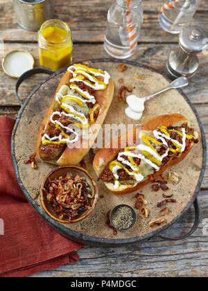 Chili Hot Dogs garniert mit gebratenen Zwiebeln, Senf und Mayonaise Stockfoto