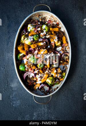 Gebratene süße Kürbis, Rosenkohl, aromatisiert mit Gewürzen und warf mit wildem Reis garniert mit Speckwürfeln und eine Zitrone Creme fraiche Dressing Stockfoto