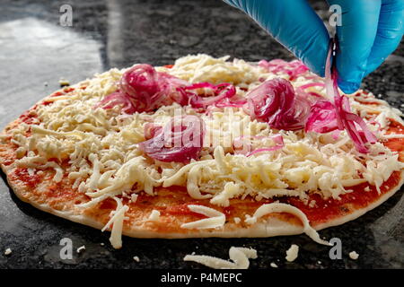 Hand mit Handschuh Verbreitung Zwiebel über den Käse pizza Stockfoto