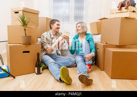 Foto von Mann mit einer Flasche Wein und Frau sitzt auf einem Sofa unter Kartons Stockfoto