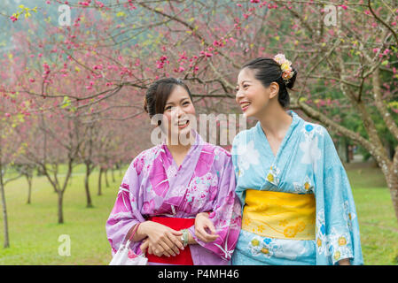 Asiatische Frauen chatten und lachen zusammen unter der Kirschblüte Baum mit ihren Händen zusammen halten. Stockfoto