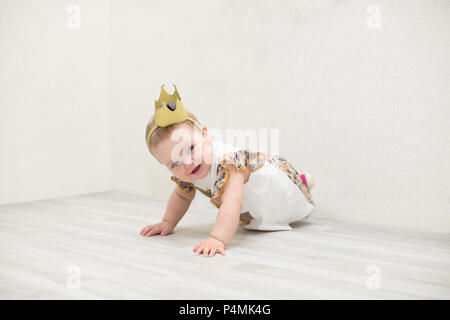 Ein 1-jähriges Mädchen mit einer Krone. Die kleine Prinzessin kriecht auf dem Boden Stockfoto