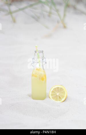 Eine Flasche Limonade mit Zitrone im Sand Stockfoto