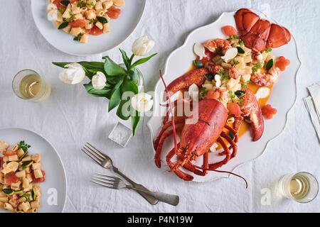 Hummer mit Rigatoni auf einem Tisch, dekoriert mit einer Vase mit Tulpen (von oben gesehen) Stockfoto