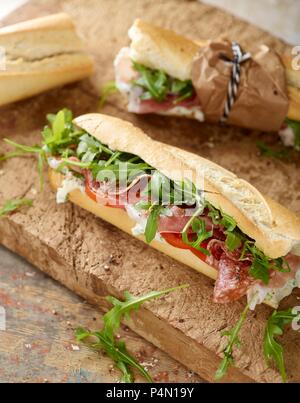 Rustikales Baguette mit Serrano Schinken, Salami, Rucola und Tomaten Stockfoto