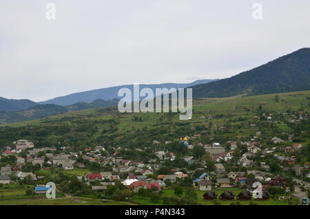 Eine wunderschöne Aussicht auf das Dorf Mezhgorye, Karpaten Region. Eine Menge von Wohngebäuden durch hohe Wald Berge und lange Fluss umgeben Stockfoto