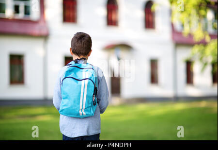 Junge mit Rucksack infront von einem Schulgebäude Stockfoto