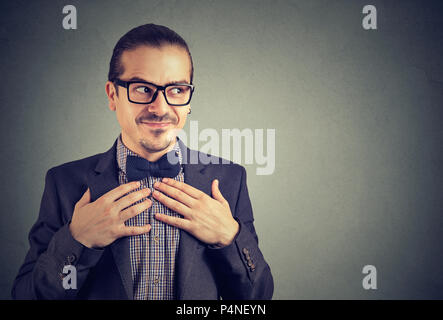 Junge Mann in Gläsern und Anzug auf der Suche nerdy entfernt, Hände auf die Brust in Schüchternheit auf grauem Hintergrund Stockfoto