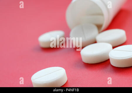 Mehrere weiße Tabletten fallen aus dem Kunststoff Glas auf die rote Fläche. Hintergrundbild über medizinische und pharmazeutische Themen. Stockfoto