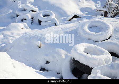 Benutzt und weggeworfen Autoreifen liegen auf der Seite der Straße, mit einer dicken Schicht Schnee bedeckt. Stockfoto