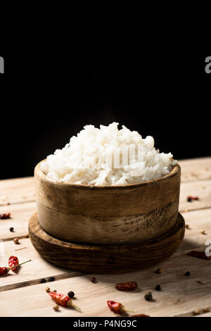 Nahaufnahme eines Buchsbaum Schüssel mit etwas gekochter Langkornreis, auf einem rustikalen Holztisch, auf einem schwarzen Hintergrund, mit einigen leeren Raum auf der Oberseite Stockfoto