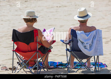 Bournemouth, Dorset, Großbritannien. Juni 2018. Wetter in Großbritannien: Schöner, heißer, sonniger Morgen an den Stränden von Bournemouth, wenn Besucher früh am Meer sind, um einen Platz zu bekommen, bevor es später voll wird und um das Beste aus der Sonne zu machen, wenn die Temperaturen für die Hitzewelle steigen. Ältere Pärchen mit Hüten auf Stühlen sitzen mit Frau Zeitung Magazin lesen - Rückansicht, Rückansicht. Quelle: Carolyn Jenkins/Alamy Live News Stockfoto