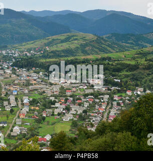 Eine wunderschöne Aussicht auf das Dorf Mezhgorye, Karpaten Region. Eine Menge von Wohngebäuden durch hohe Wald Berge und lange Fluss umgeben Stockfoto