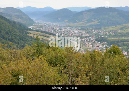 Eine wunderschöne Aussicht auf das Dorf Mezhgorye, Karpaten Region. Eine Menge von Wohngebäuden durch hohe Wald Berge und lange Fluss umgeben. Stockfoto