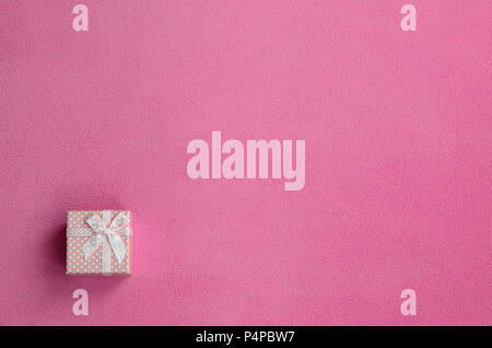 Ein kleines Geschenk Box in Rosa mit einer kleinen Verbeugung liegt auf einer Decke aus weichem, flauschigen Rosa fleece Stoff. Verpackung für ein Geschenk für Ihre reizende Freundin. Stockfoto