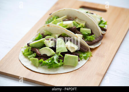 Mais Tortillas mit gegrilltem Rindfleisch, Avocado und Salat auf Holzbrett, Nahaufnahme. Von der Seite. Stockfoto