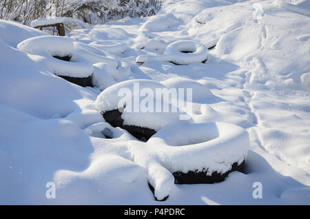 Benutzt und weggeworfen Autoreifen liegen auf der Seite der Straße, mit einer dicken Schicht Schnee bedeckt. Stockfoto