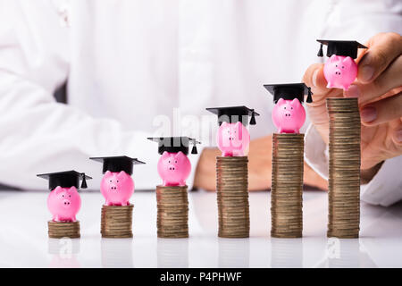 Nahaufnahme der Hand einer Person sparschwein mit Graduierung Hut auf Gestapelte Münzen Stockfoto