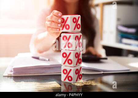 Die Geschäftsfrau Hand Stapeln würfelförmige Blöcke mit roten Prozentsatz Symbol über Schreibtisch Stockfoto