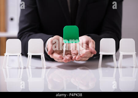 Unternehmer mit grünen Sitz unter weißen Stühlen Stockfoto