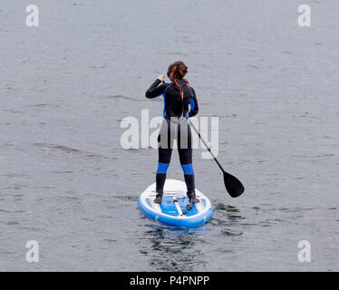 Eine Frau im Anzug auf dem SUP board schwimmt im Meer. SUP-boarding ist beliebte Art von Surfen Sport. Sport und Hobby. Stockfoto